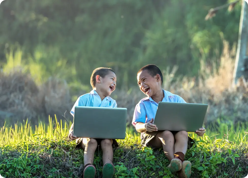 Two children laughing facing each other while holding laptops